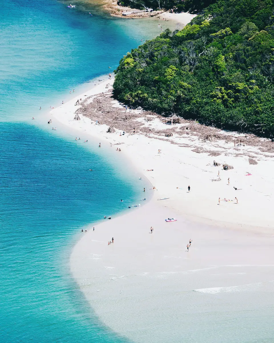 White sandy beach with turquoise water and a green headland in Australia.