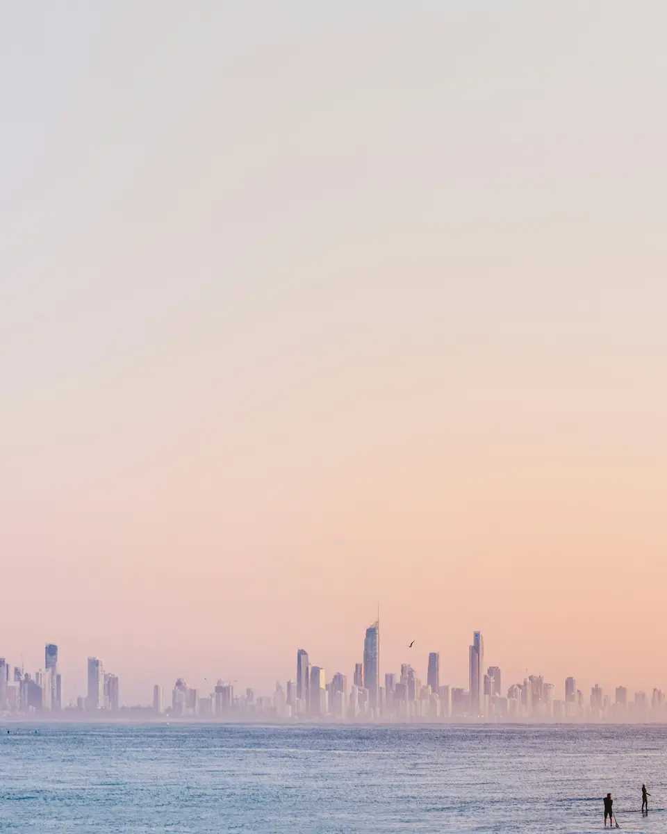 View across the water to a distant skyline with a pastel sky and small figures on the shore in Australia.