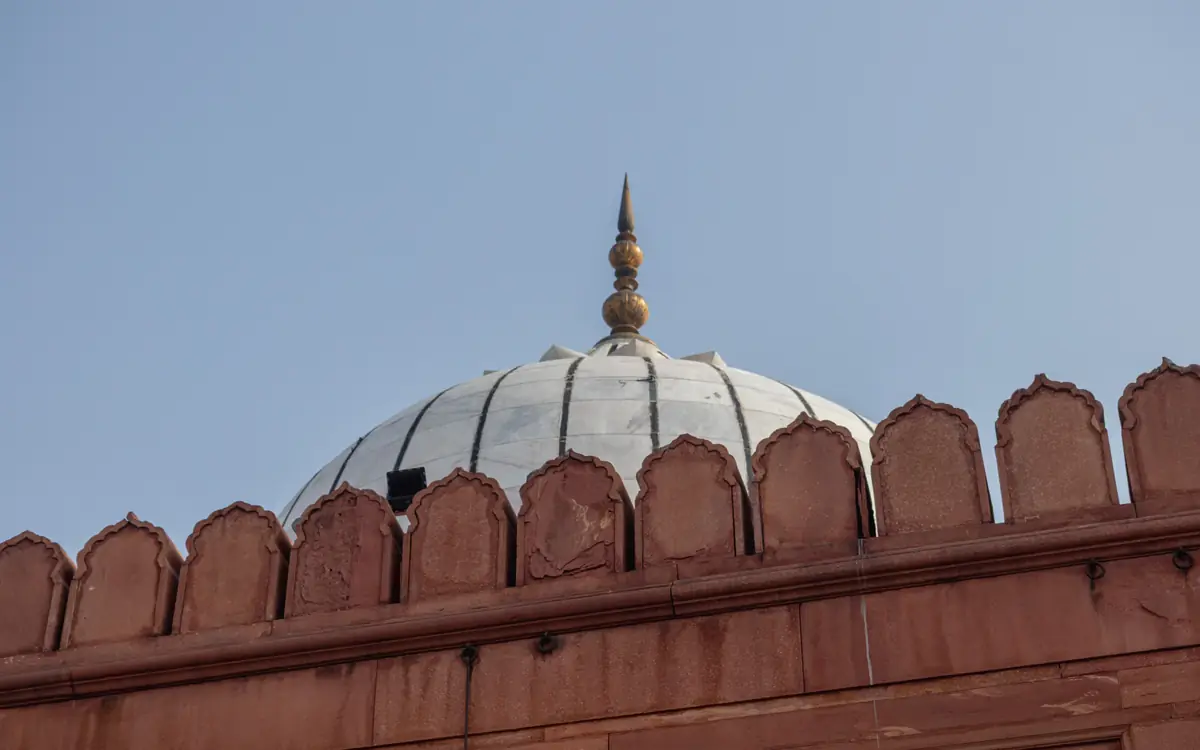 White dome and finial behind a red sandstone parapet under clear sky in Delhi.
