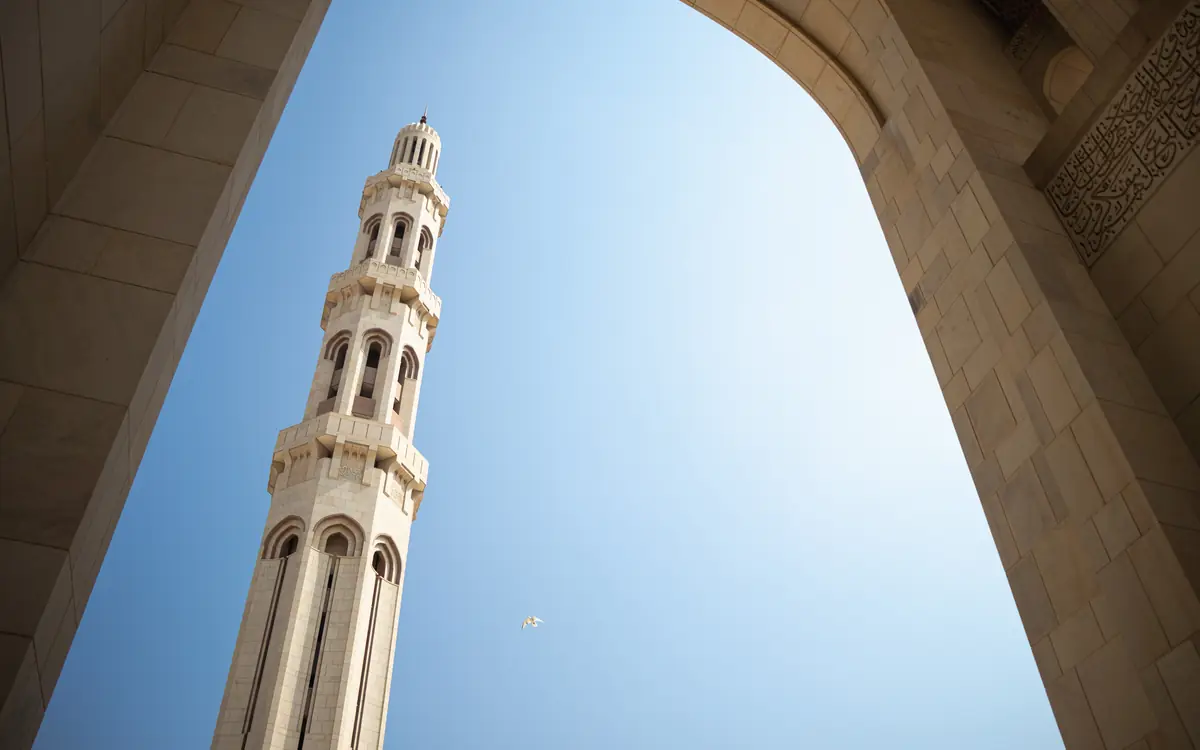 Tall pale minaret seen through a clean arched foreground frame in Muscat.