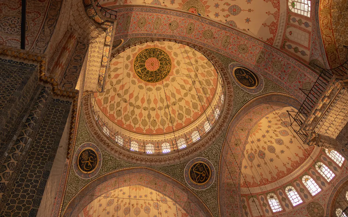 Decorated mosque dome with painted patterns, arched windows, and calligraphy medallions in Istanbul.