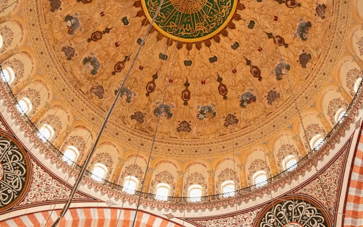 Ornate mosque dome with calligraphy medallions, arched windows, and decorative ribs in Istanbul.