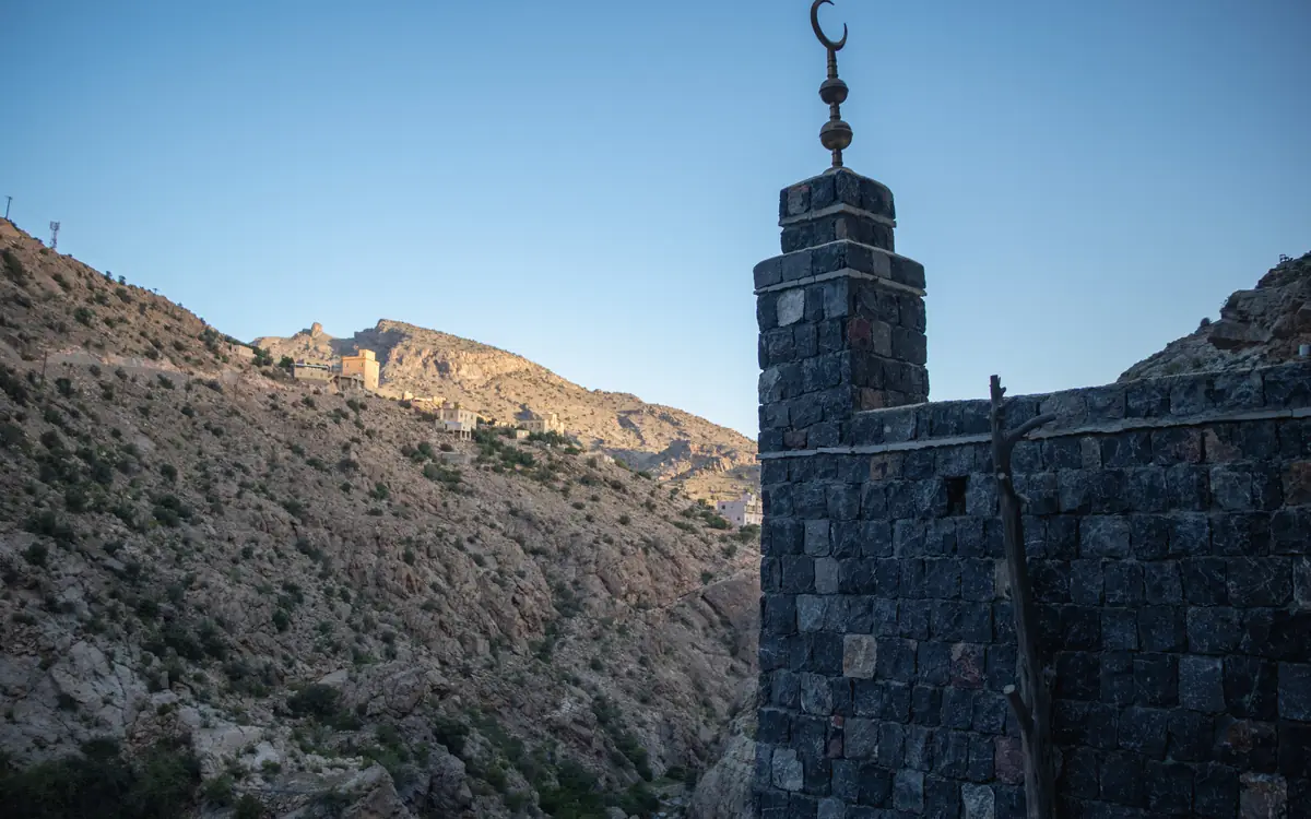 Stone structure with a small crescent-topped element in a rocky Oman mountain valley.
