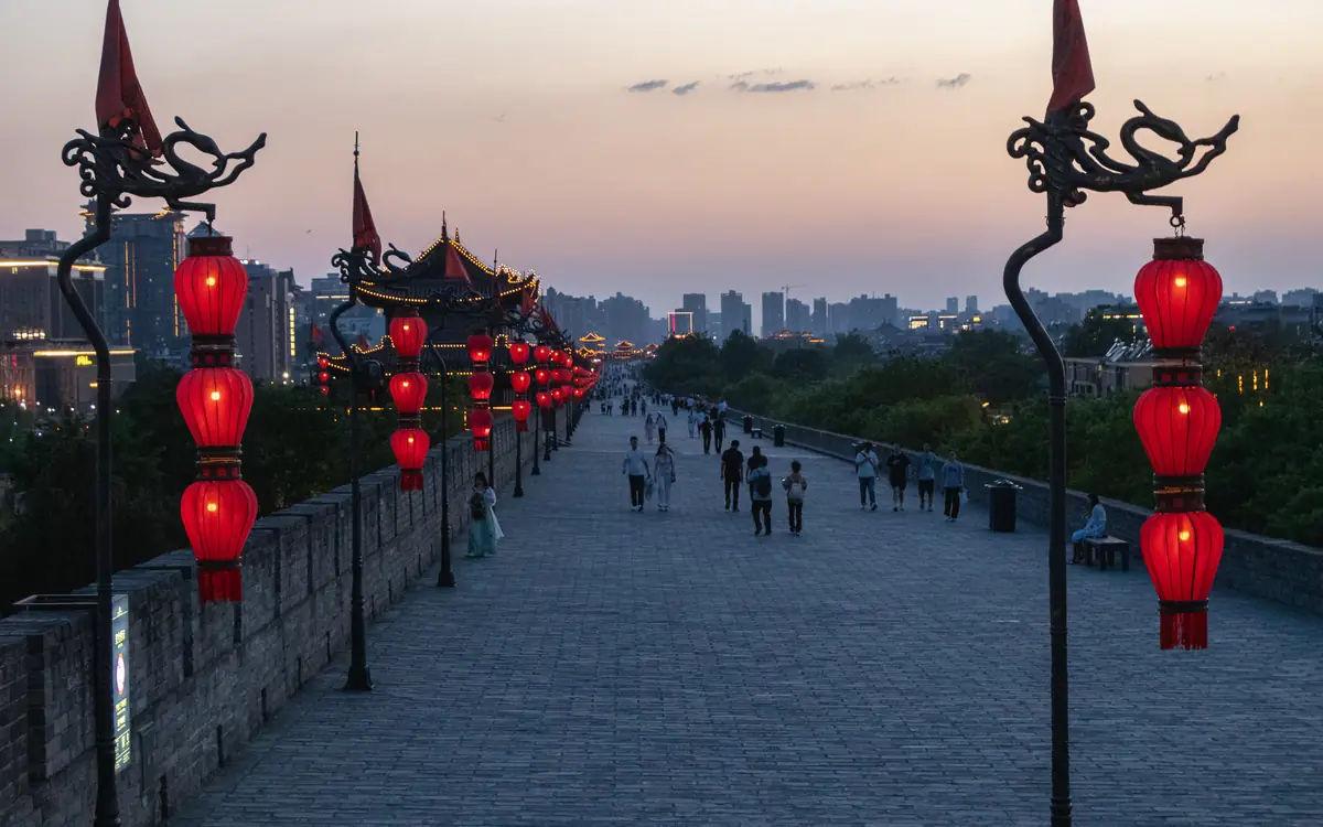 City wall walkway in China lined with red lanterns, lamp posts, and traditional rooflines.
