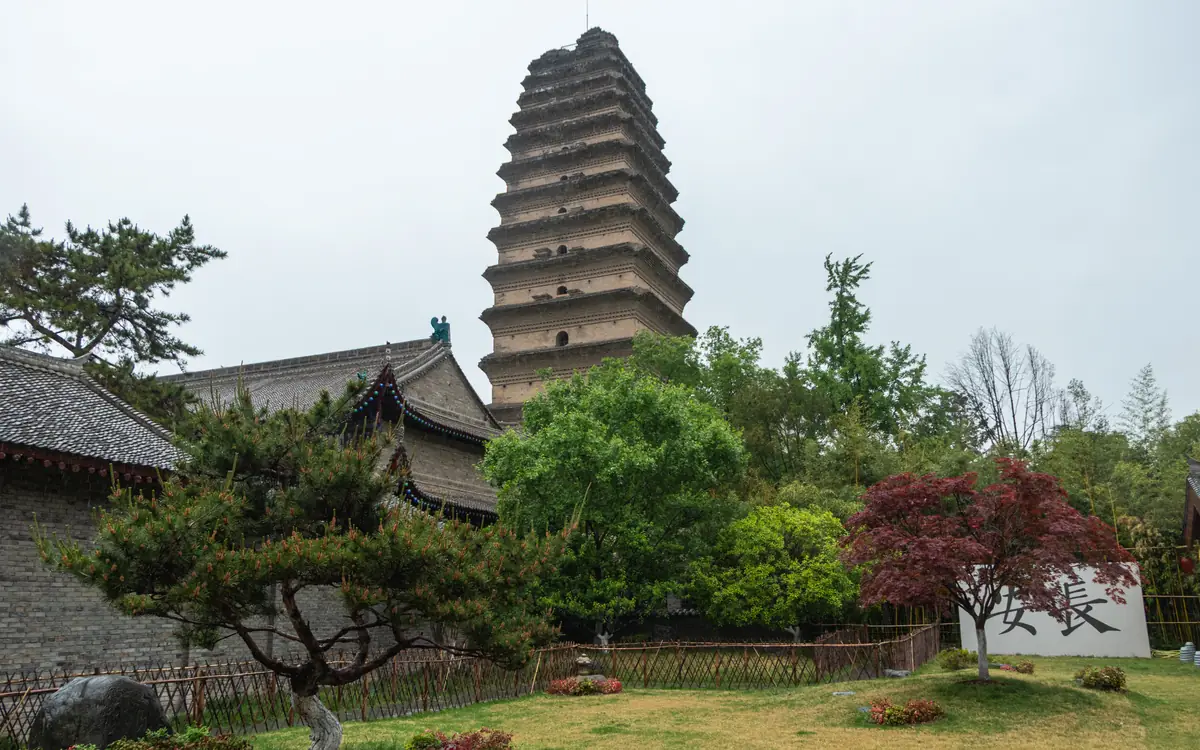 Tiered brick pagoda with temple roofs and garden trees in Sichuan.