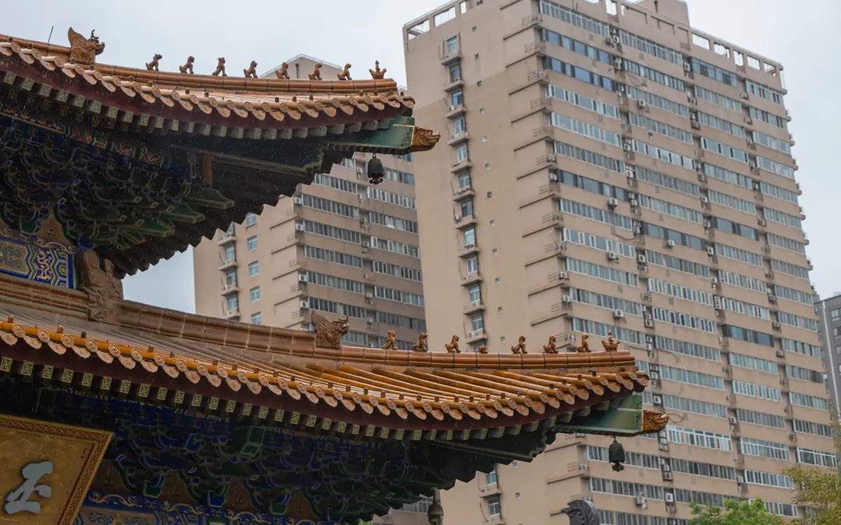 Chinese temple roof eaves and painted brackets in front of modern high-rise apartments in Sichuan.