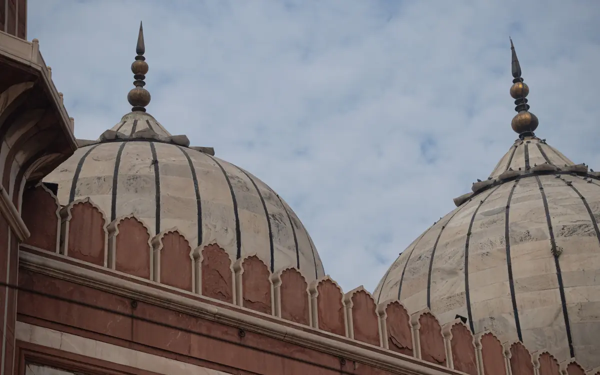 Large pale domes, slender finials, and red sandstone architecture in Delhi.
