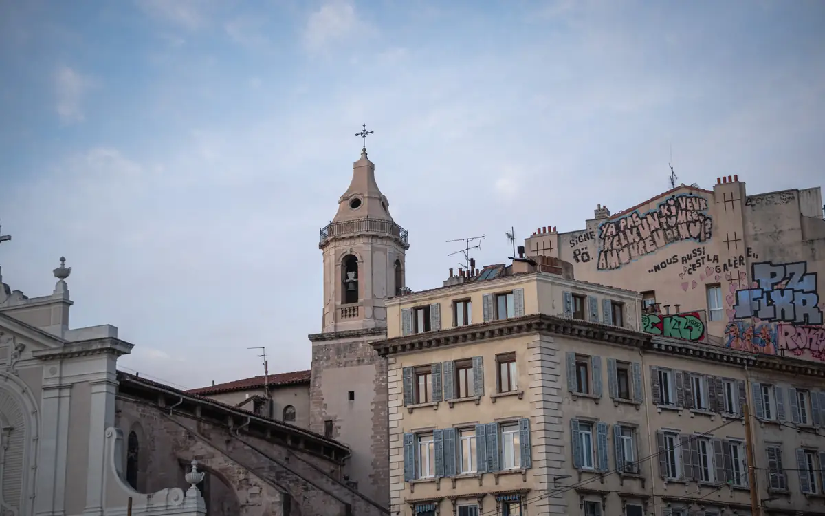 Church bell tower, older urban buildings, graffiti, and shuttered windows in Marseille.