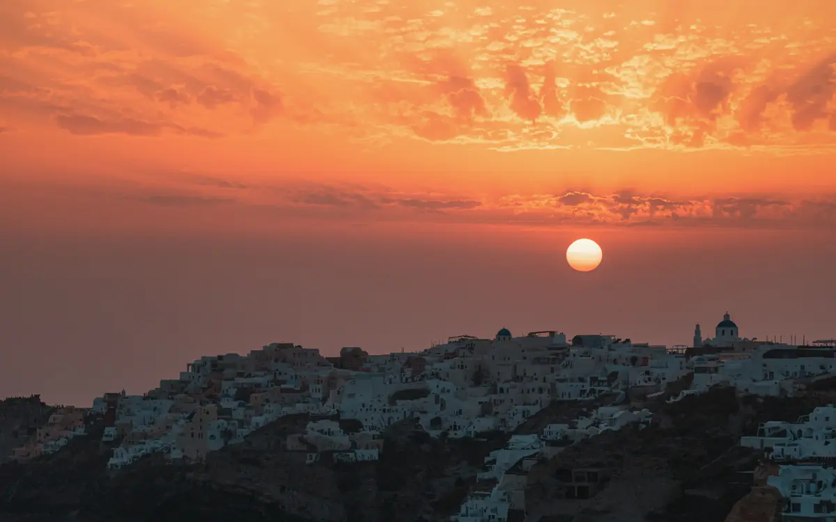 Whitewashed island town silhouette with a dome and clustered buildings at sunset in Greece.