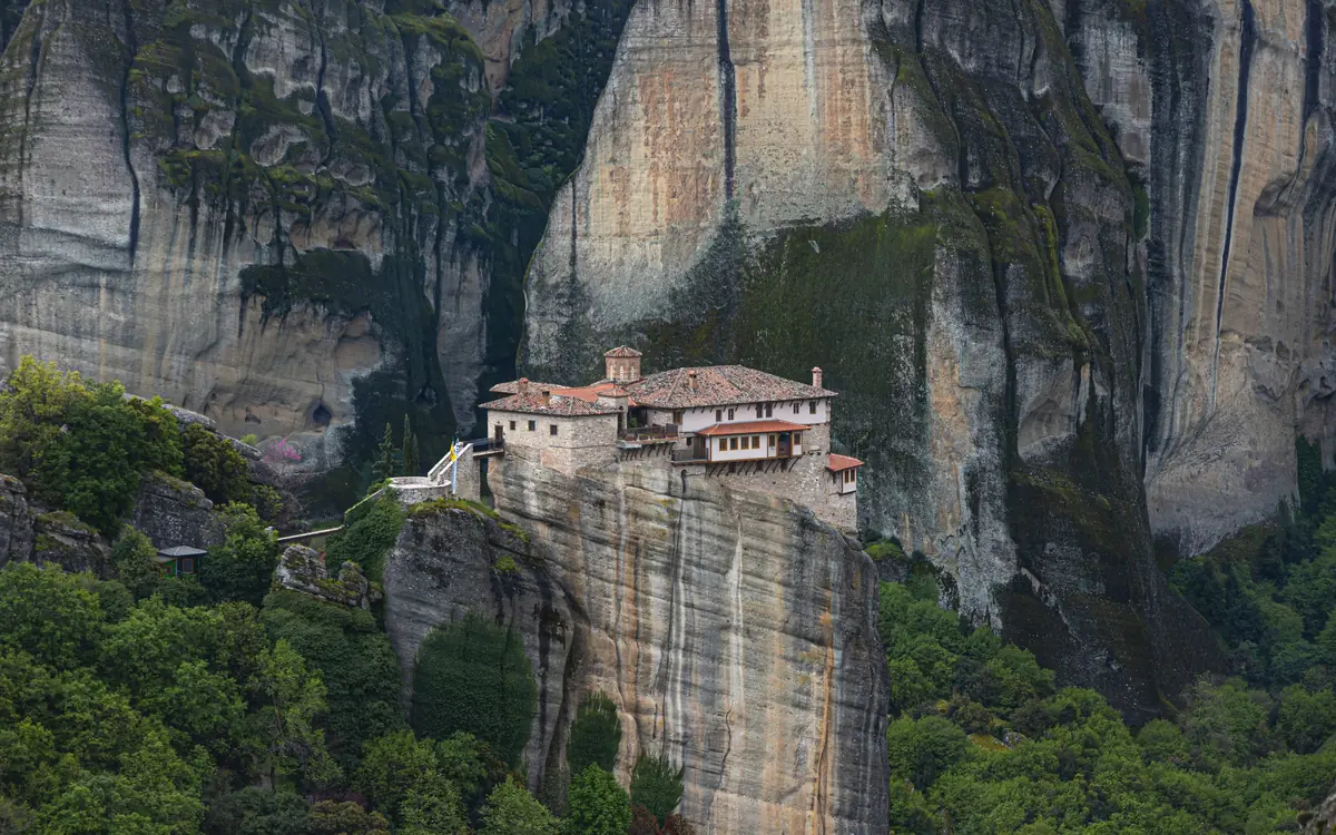 Meteora monastery on a sheer rock pillar above forest.