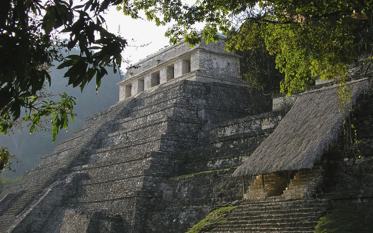 A stone Maya temple partly framed by trees at an archaeological site in Chiapas.