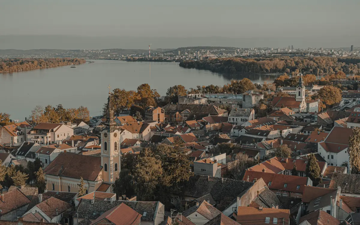 Belgrade river view with red-roofed buildings, church towers, and hazy distant hills.