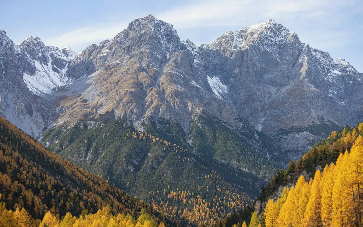 Gray mountain peaks, snow patches, and autumn-colored forest in Switzerland.