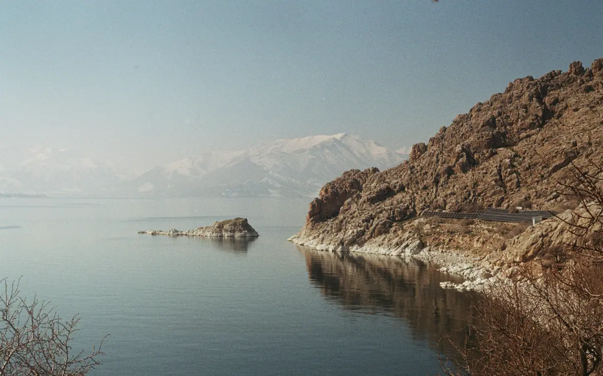 Rocky lakeshore or sea edge with calm water and faint snowy mountains in Turkey.