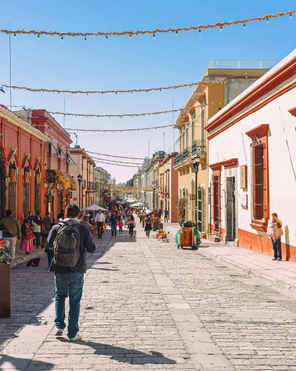 Colourful street with low buildings, a pedestrian, and decorative bunting overhead in Mexico.