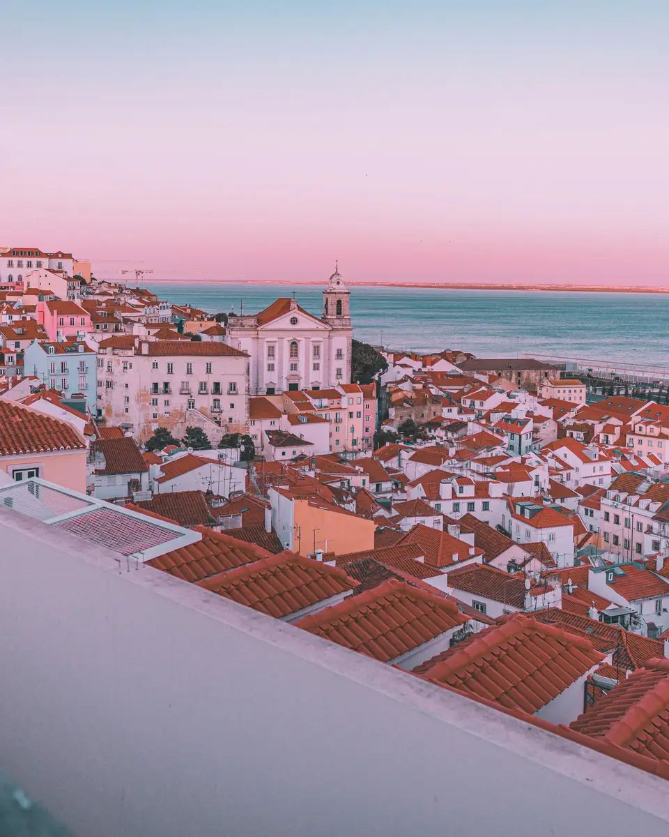 Whitewashed coastal town with a church, rooftops, and a pink sunset sky over the water in Portugal.