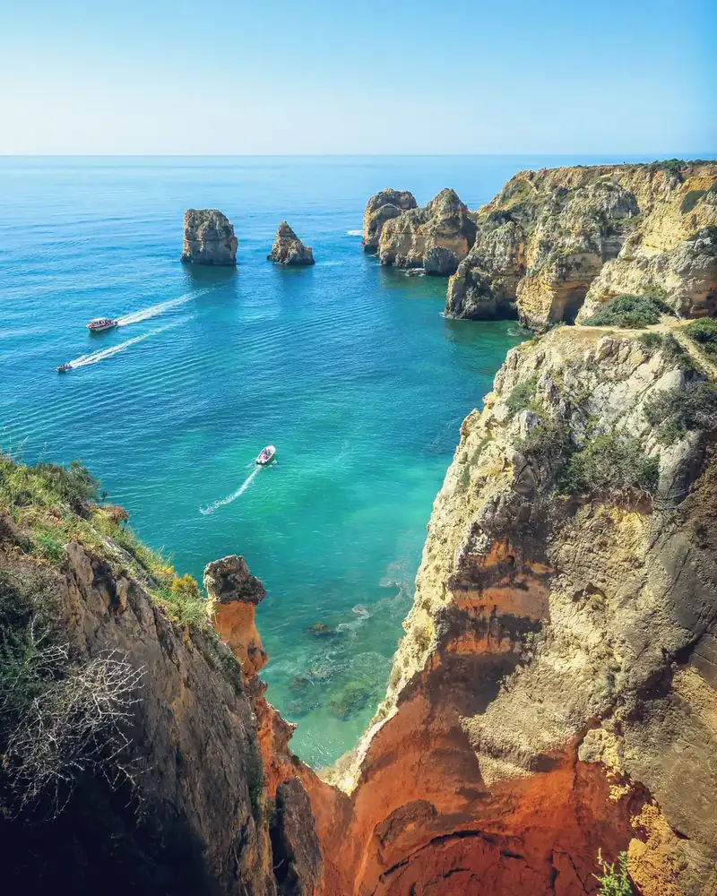 Cliff coastline with boats on bright blue water and rock formations in Portugal.